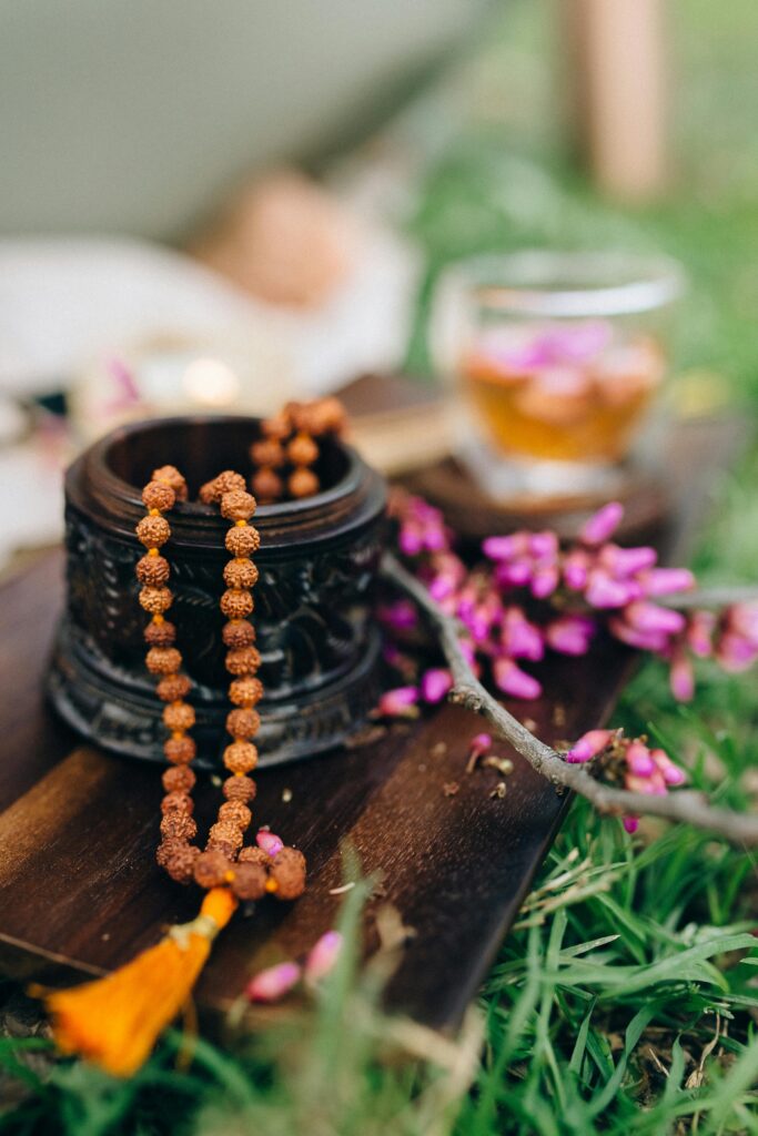 Tranquil meditation setup with wooden mala beads, tea, and flowers on grassy surface.